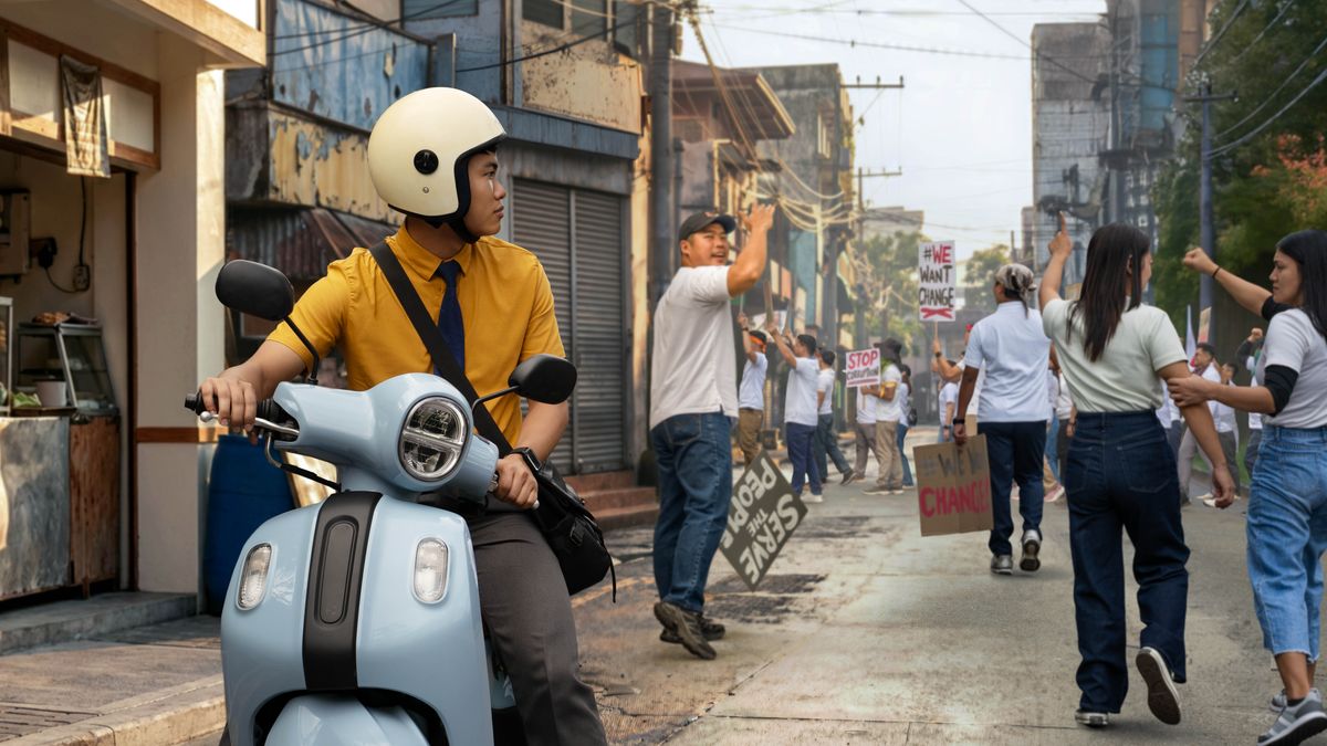 A young brother on a motorbike looking at a group of protesters. One protester gestures for the brother to join them.