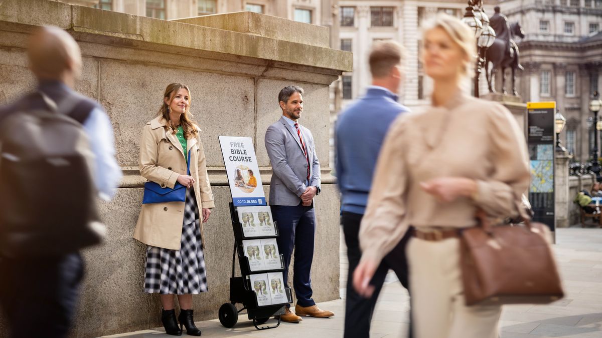 A couple stand beside a literature cart on a busy sidewalk.