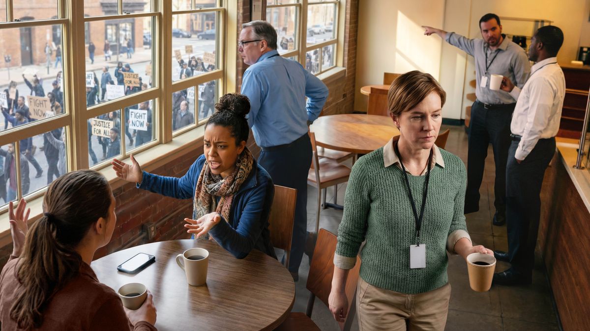 A sister leaves a break room as her coworkers argue and gesture toward a protest happening outside the window.